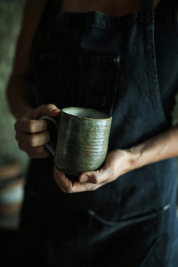 A woman in a blue apron holding a green coffee mug