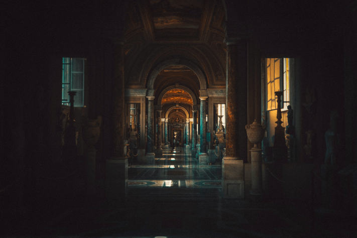 A well-lit hallway adorned with statues, illuminated by natural light streaming through the windows.