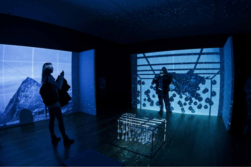 People standing in front of a large screen with blue lights illuminating the scene.
