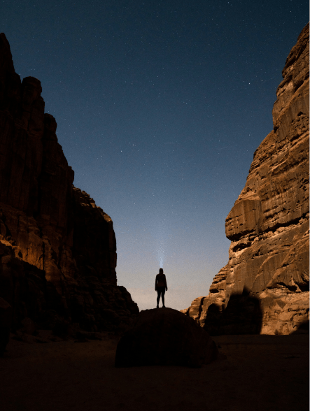 A man standing on a rock in the desert at night, gazing at the starry sky.